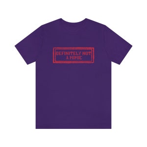 May include: Purple t-shirt with a red rectangular stamp that says "DEFINITELY NOT A MIMIC".