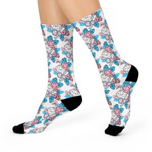May include: A pair of white socks with a pattern of pink and blue 20-sided dice, also known as D20s, surrounded by crystals. The socks are black at the toe and heel.