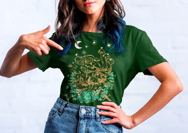 May include: A green t-shirt with a gold and green mushroom design and a green twenty-sided die. The shirt has a crescent moon and stars in the top left corner.