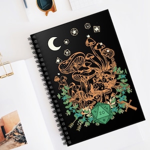 May include: A black spiral notebook with a design of orange mushrooms, green leaves, and a green 20-sided die on a black background. The design also includes a crescent moon and stars.