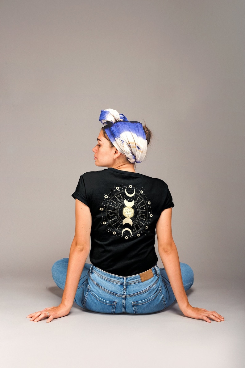 May include: A black t-shirt with a gold moon and stars design on the back. The design features a crescent moon, a full moon, and a crescent moon with a star inside. The design is surrounded by a circle of stars.
