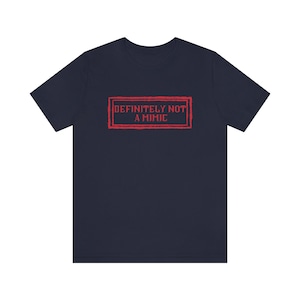 May include: A navy blue t-shirt with a red stamp that says "DEFINITELY NOT A MIMIC".