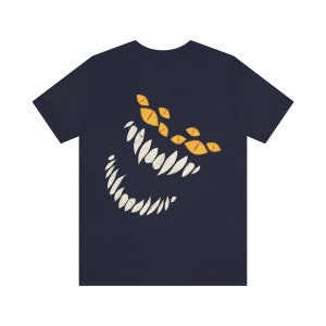 May include: A navy blue t-shirt with a graphic of a white, toothy grin and yellow eyes. The graphic is stylized to look like a monster.
