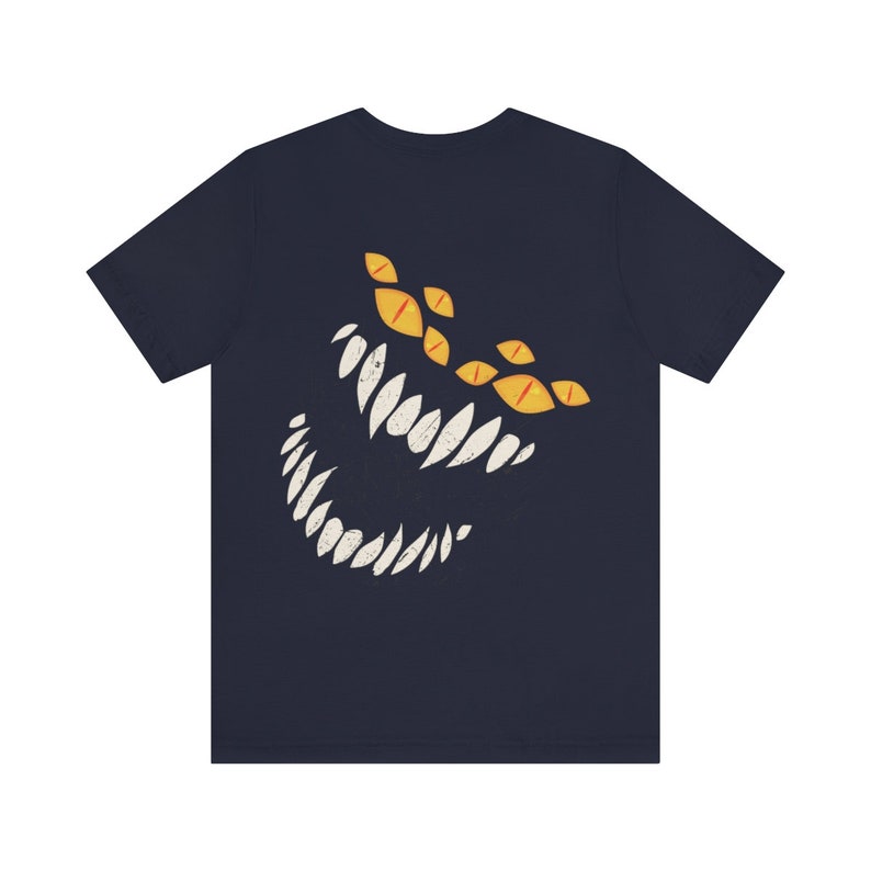 May include: A navy blue t-shirt with a graphic of a white, toothy grin and yellow eyes. The graphic is stylized to look like a monster.