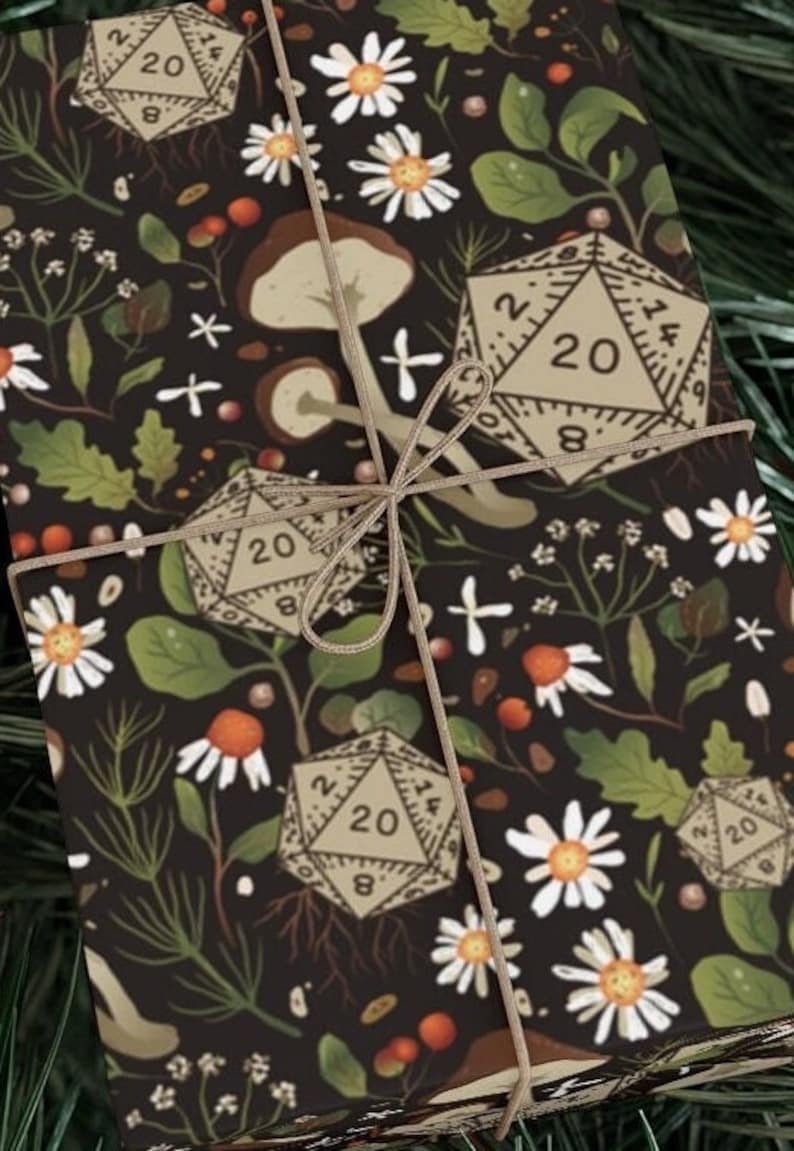 May include: Gift-wrapped package with a dark background featuring a botanical pattern of daisies, leaves, mushrooms, and D20 dice. The package is tied with twine, creating a rustic and whimsical aesthetic.