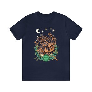 May include: Navy blue t-shirt with a graphic of mushrooms, a crescent moon, stars, and a green twenty-sided die. The graphic is surrounded by green foliage.