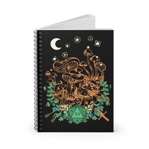 May include: A black spiral notebook with a design of mushrooms, a crescent moon, and a green 20-sided die. The mushrooms are orange and white, and the die has white numbers on a green background.