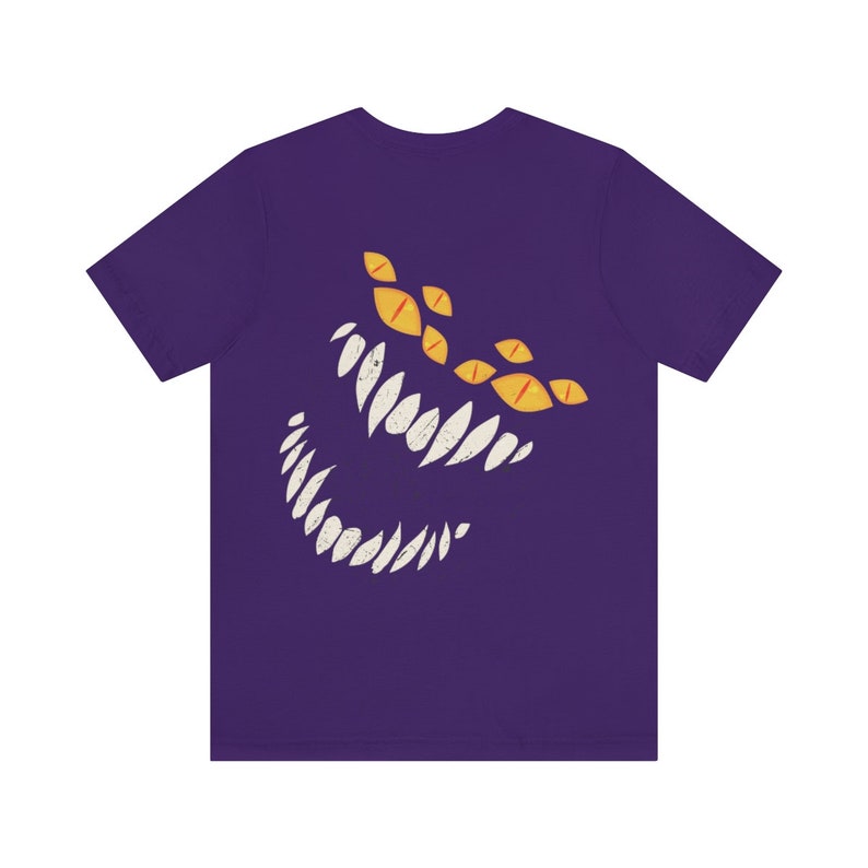 May include: Purple t-shirt with a white and yellow graphic of a monster's face with sharp teeth and multiple eyes.