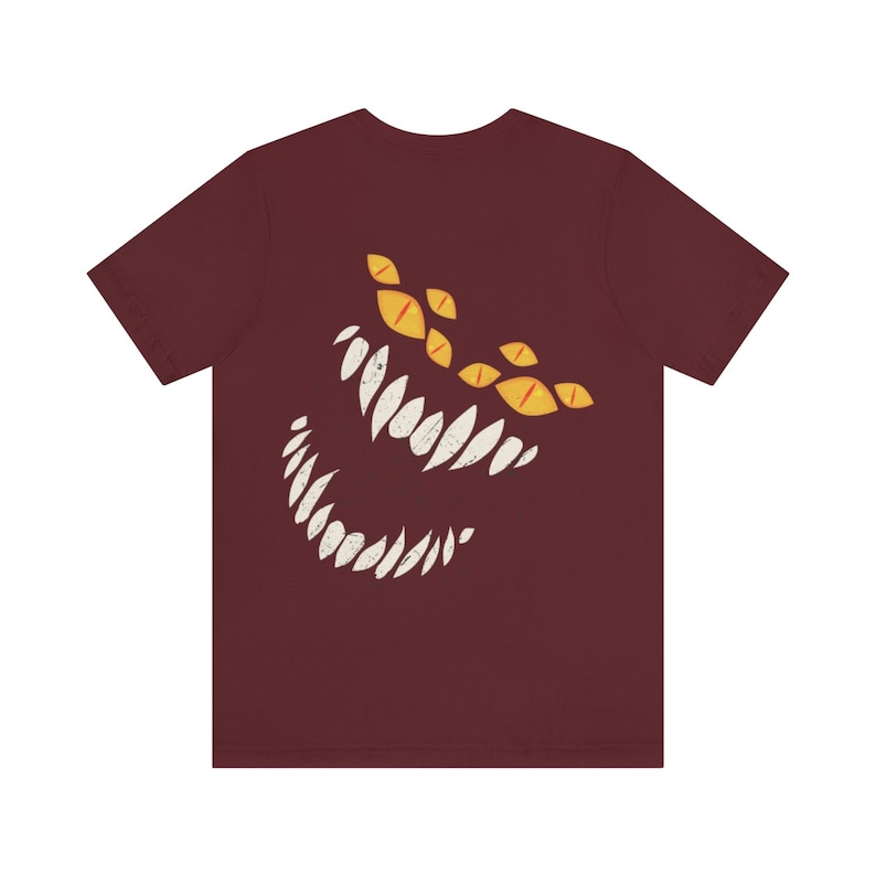 May include: A maroon t-shirt with a white and yellow graphic of a monster's face with sharp teeth and multiple eyes.