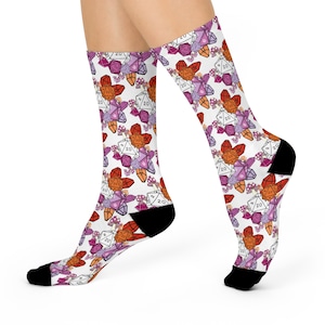 May include: A pair of white socks with a pattern of colorful 20-sided dice and crystals. The dice are red, orange, purple, and pink. The socks are a fun and quirky way to show your love of Dungeons and Dragons.