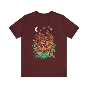 May include: A maroon t-shirt with a graphic of a cluster of mushrooms, a crescent moon, stars, and a green 20-sided die.