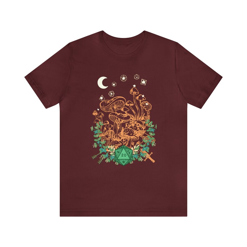 May include: A maroon t-shirt with a graphic of a cluster of mushrooms, a crescent moon, stars, and a green 20-sided die.
