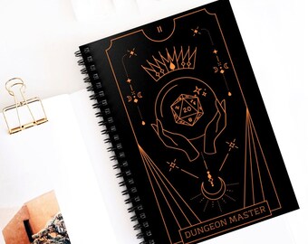 May include: A black spiral bound notebook with a gold design. The cover features a crown, a 20-sided die, and the words "Dungeon Master".