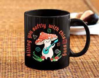 May include: Black coffee mug with a white mushroom character playing a guitar. The text on the mug reads "Killing you softly with this song".