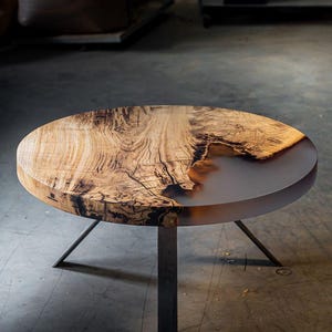May include: A round wooden table with a clear epoxy resin inlay. The table has three black metal legs.