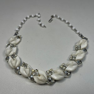 May include: A white vintage necklace with a chain and a series of white flower-shaped pendants with silver accents and clear rhinestones.