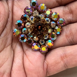 May include: A gold-toned brooch with a cluster of iridescent rhinestones in shades of pink, orange, and yellow.