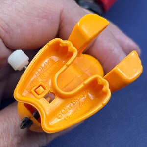 May include: Close-up of an orange plastic toy with a wind-up mechanism. The toy has a wing-like design and the text "TOMY MADE IN CHINA" is visible. The toy is a vintage Disney collectible.