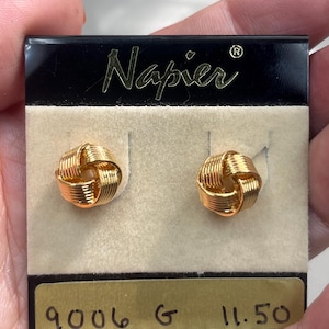 Puede incluir: Pendientes de nudo Napier en tono dorado en una tarjeta negra y blanca con el texto "Napier" y "9006 G 11.50".