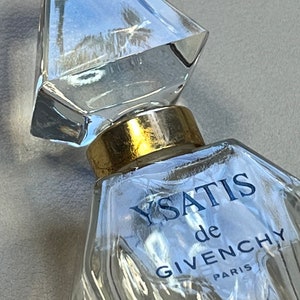 May include: A clear glass bottle of Ysatis de Givenchy perfume with a gold cap and a diamond-shaped stopper. The bottle has a textured surface and the label reads "Ysatis de Givenchy Paris".