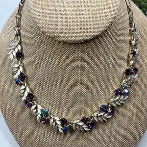 May include: A gold tone necklace with a leaf design and purple iridescent rhinestones.