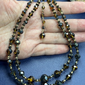 May include: A vintage two-strand necklace with faceted amber beads and gold-tone details. The necklace has a delicate chain and a decorative drop pendant. The beads vary in size and shape, creating a textured appearance.