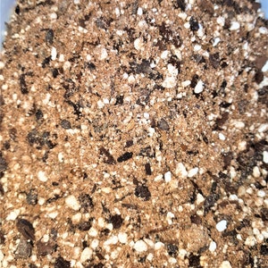 May include: Close-up of a mixture of brown and white soil. The soil is made up of small particles and larger pieces of bark.