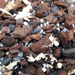 May include: A close-up of a mixture of brown bark chips, black charcoal pieces, and white pebbles. This is a common soil amendment for plants.