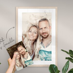 May include: A framed watercolor painting of a couple. The painting is in a light wood frame and has a white mat. The couple is smiling and looking at the camera. The background of the painting is a light brown color with white and blue watercolor splatters.