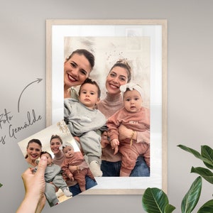 May include: A framed photo of two women and two babies. The women are smiling and holding the babies. The babies are wearing matching outfits with their names on them. The photo is in a white frame with a white mat.
