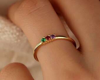 May include: A gold ring with three small gemstones: a green, a red, and a purple stone.