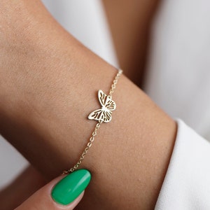 May include: A delicate gold chain bracelet with a cutout butterfly charm. The bracelet is on a person's wrist.
