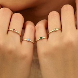 May include: Four gold rings with small colored gemstones. The rings are worn on the fingers of a person's hands.