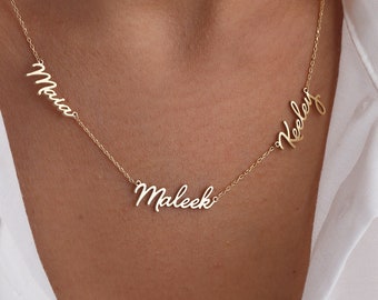 May include: A gold-colored necklace with three name pendants: "Maia", "Maleek", and "Keeley" in a delicate script font. The necklace is displayed against a white shirt.
