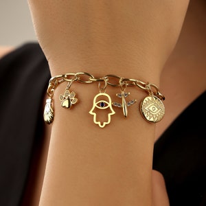 May include: A gold charm bracelet with multiple charms including a paw print, a hamsa hand with a blue eye, a dragonfly, a small shell, and two evil eye charms.
