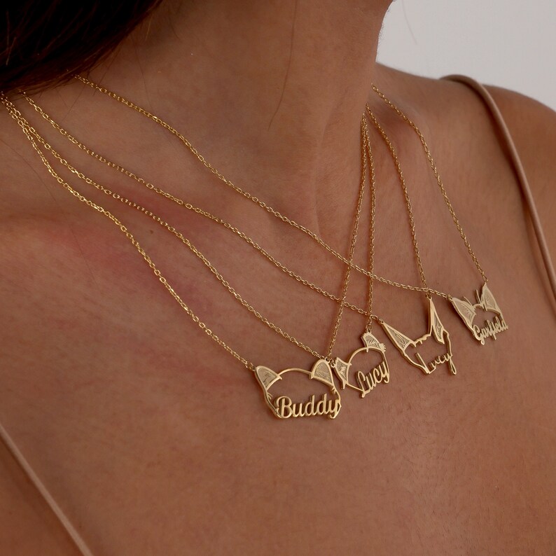 May include: Four gold necklaces with personalized nameplates. The names on the nameplates are Buddy, Lucy, Lucy, and Garfield.