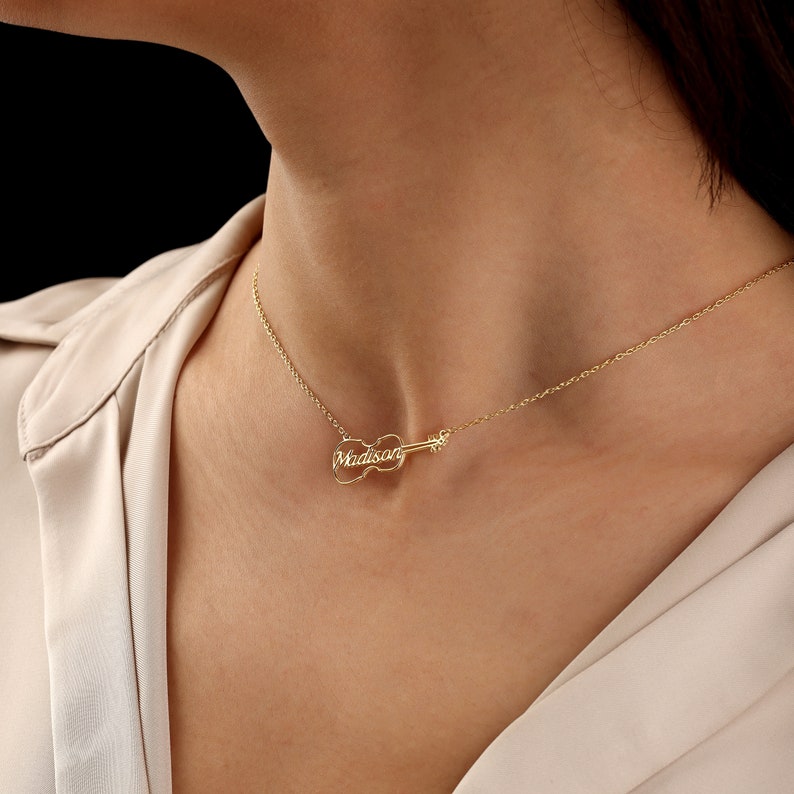 May include: A gold necklace with a violin pendant that has the name "Madison" engraved on it.
