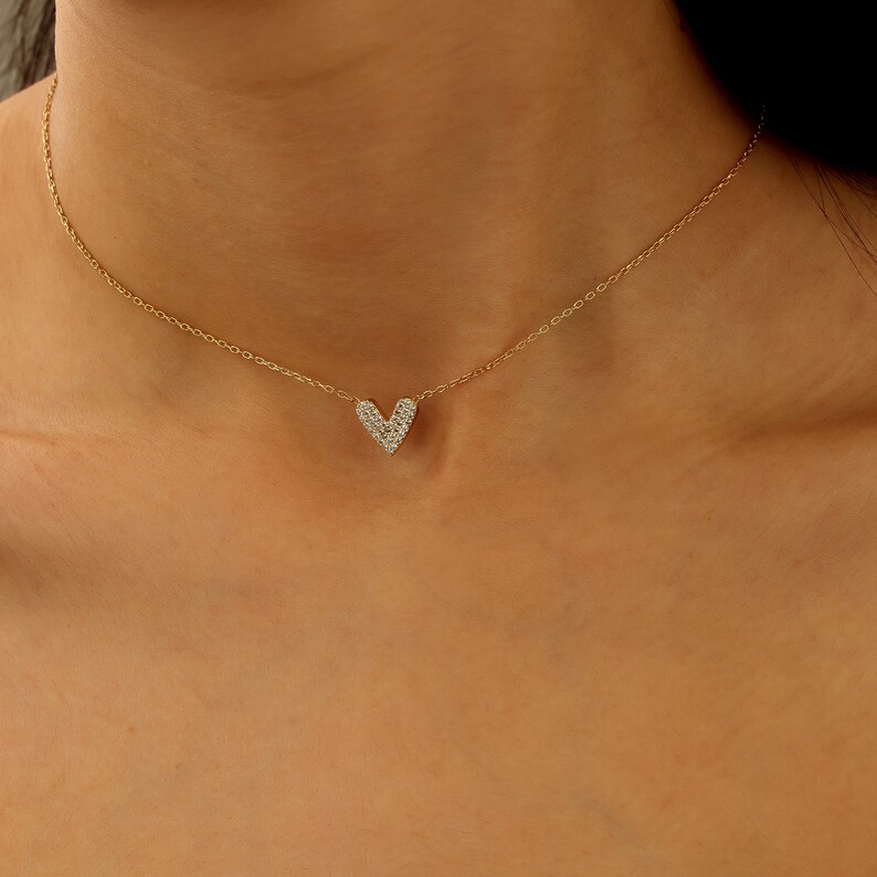 May include: A gold chain necklace with a small, heart-shaped pendant encrusted with clear cubic zirconia stones.