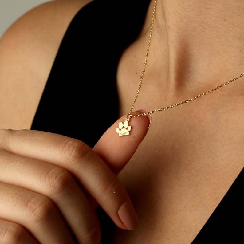 May include: Gold necklace with a paw print charm. The charm has the name "Kalie" engraved on it.