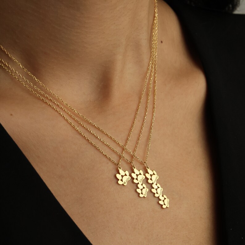 May include: Gold necklace with four paw print charms, each engraved with a different name: Millie, Charlie, Luna, and Winnie.