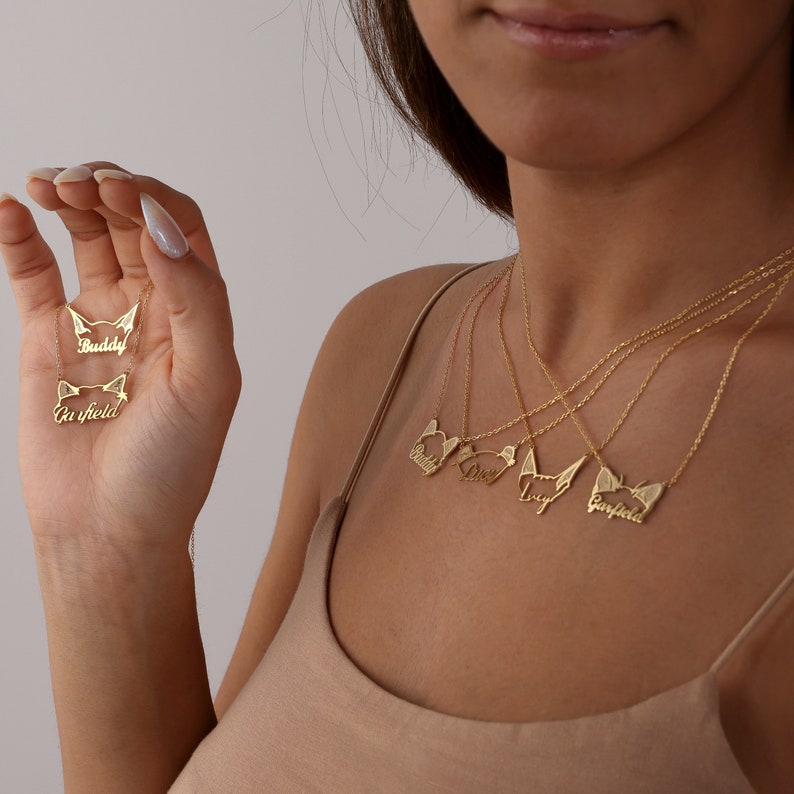 May include: A set of four gold necklaces with cat-shaped pendants. Each pendant has a different name inscribed on it: Buddy, Lucy, Max, and Garfield.