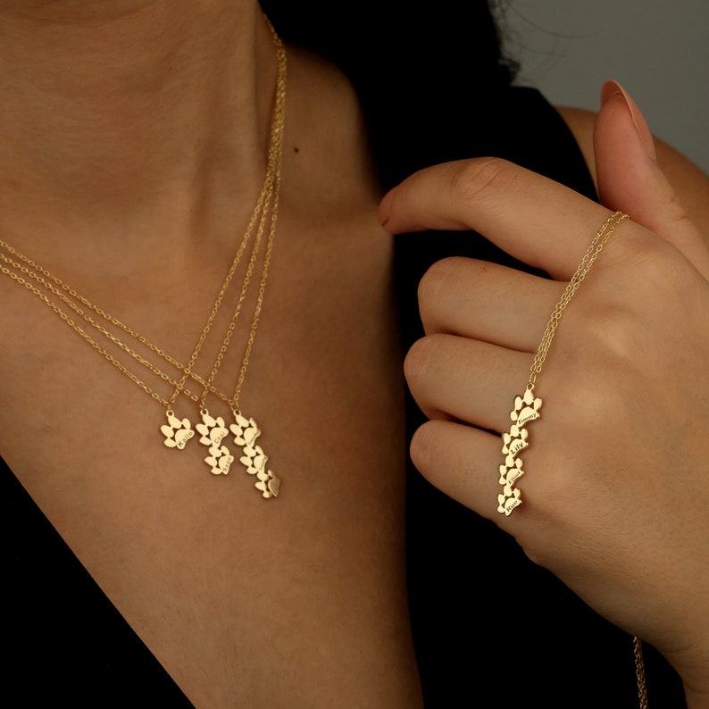May include: A gold necklace with a paw print charm. The necklace is layered with three chains and has a pendant with multiple paw prints. The pendant is in the shape of a paw print.