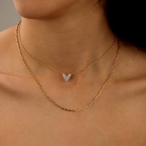 May include: A gold chain necklace with a small heart pendant encrusted with clear cubic zirconia stones. The necklace is layered over a second, thicker gold chain.