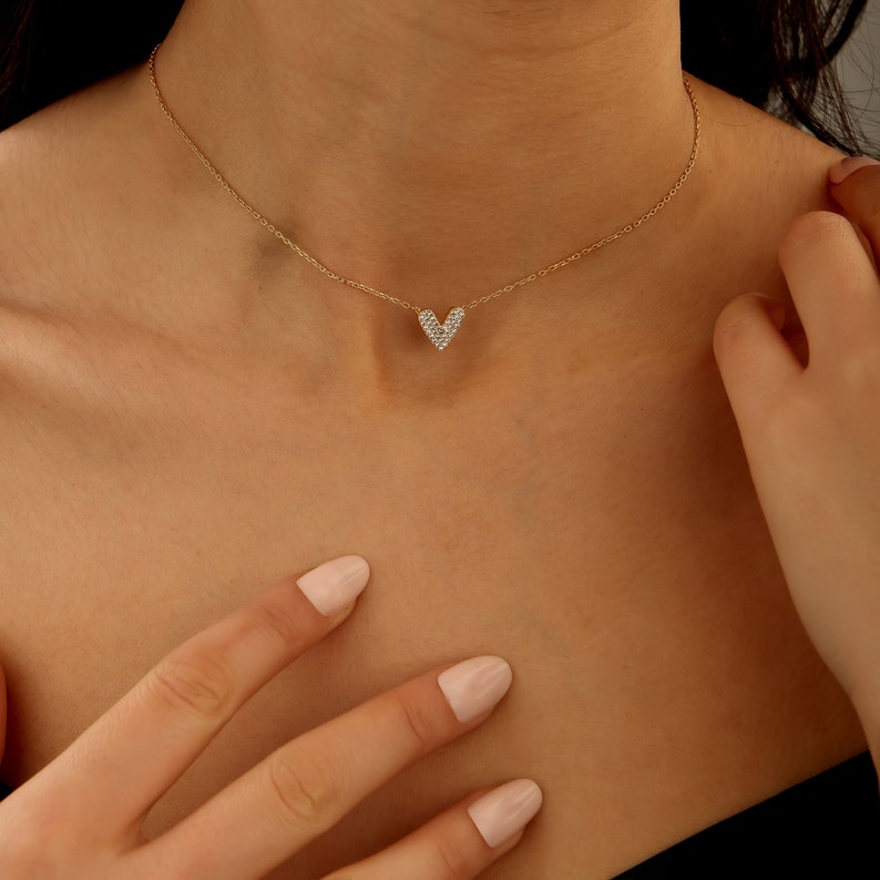May include: A gold chain necklace with a small, heart-shaped pendant encrusted with clear cubic zirconia stones.