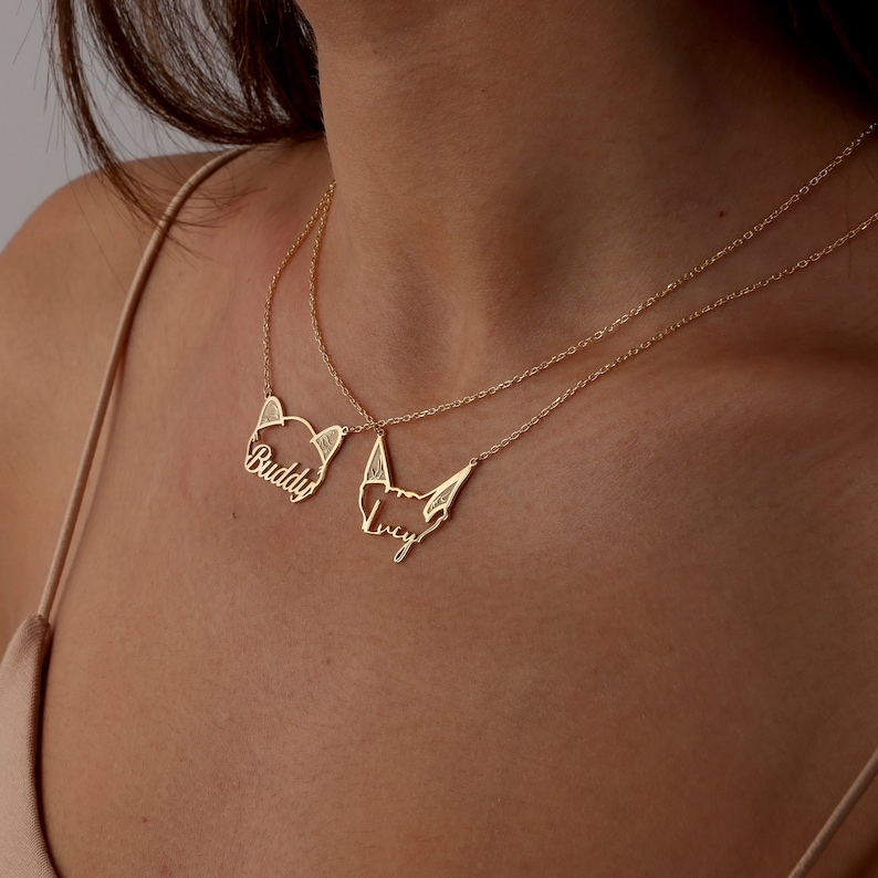 May include: Two gold necklaces with personalized name pendants. The top necklace has a pendant that says "Buddy" and the bottom necklace has a pendant that says "Lucy".