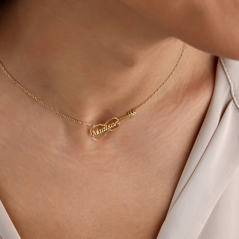 May include: A gold necklace with a violin pendant featuring the name "Madison" engraved on it.