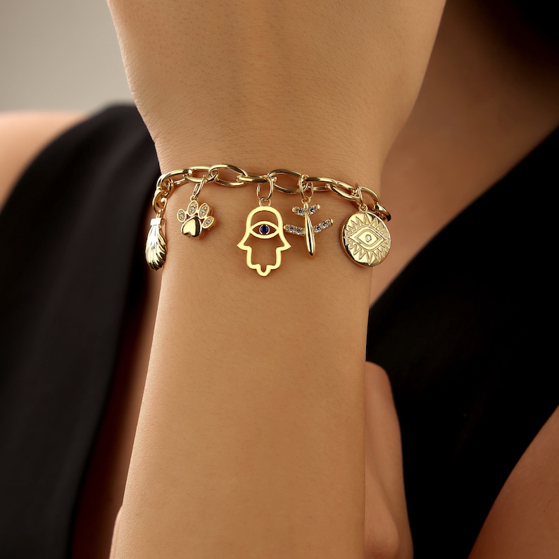 May include: A gold charm bracelet with multiple charms including a paw print, a hamsa hand with a blue eye, a dragonfly, a small shell, and two evil eye charms.