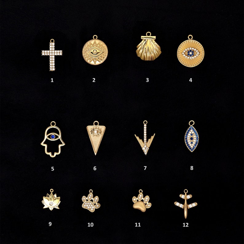 May include: Twelve gold-toned charms with various designs, including a cross, an evil eye, a seashell, a hamsa hand, a triangle, an arrow, a lotus flower, and a paw print. The charms are all set with clear and blue crystals.