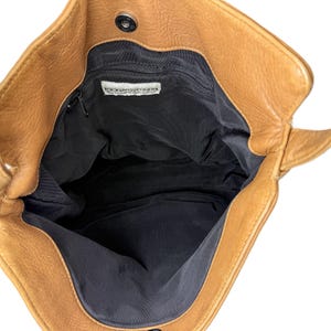 Pu&ograve; includere: Vista aperta di una borsa tote in pelle marrone con interno nero. La borsa ha una chiusura magnetica e una piccola tasca interna con cerniera. Il marchio "DONNA KARAN" &egrave; visibile su un'etichetta all'interno della borsa.