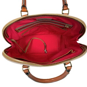 May include: Open view of a tan and brown dome-shaped handbag with brown leather handles and trim. The interior is lined with red fabric and features multiple pockets and a key clip. The bag has a gold zipper and hardware.